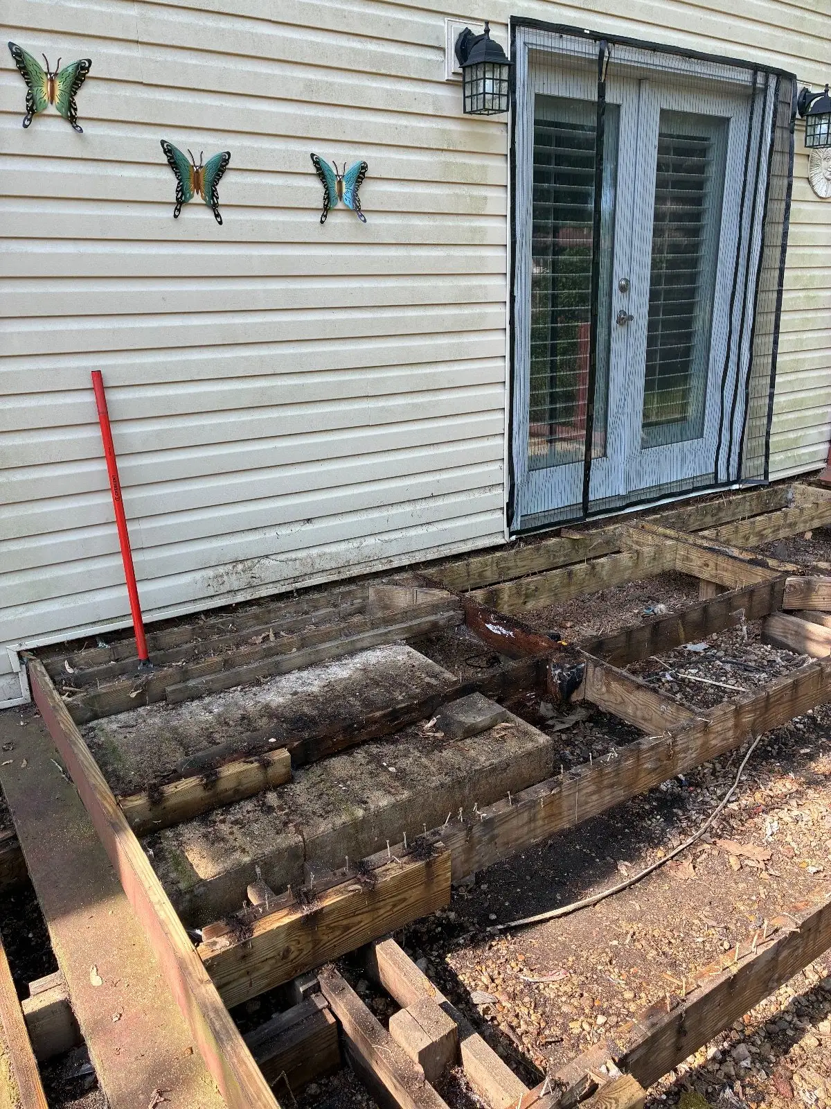The old deck half torn out, with rotted framing sitting on a brick base below the French doors