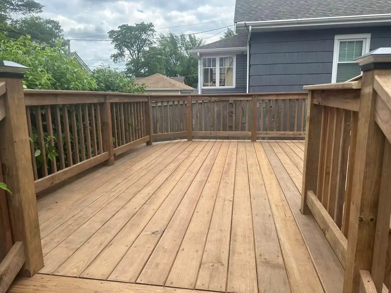 Tan wood deck with matching wood railings and a wide open surface, backing onto neighboring homes