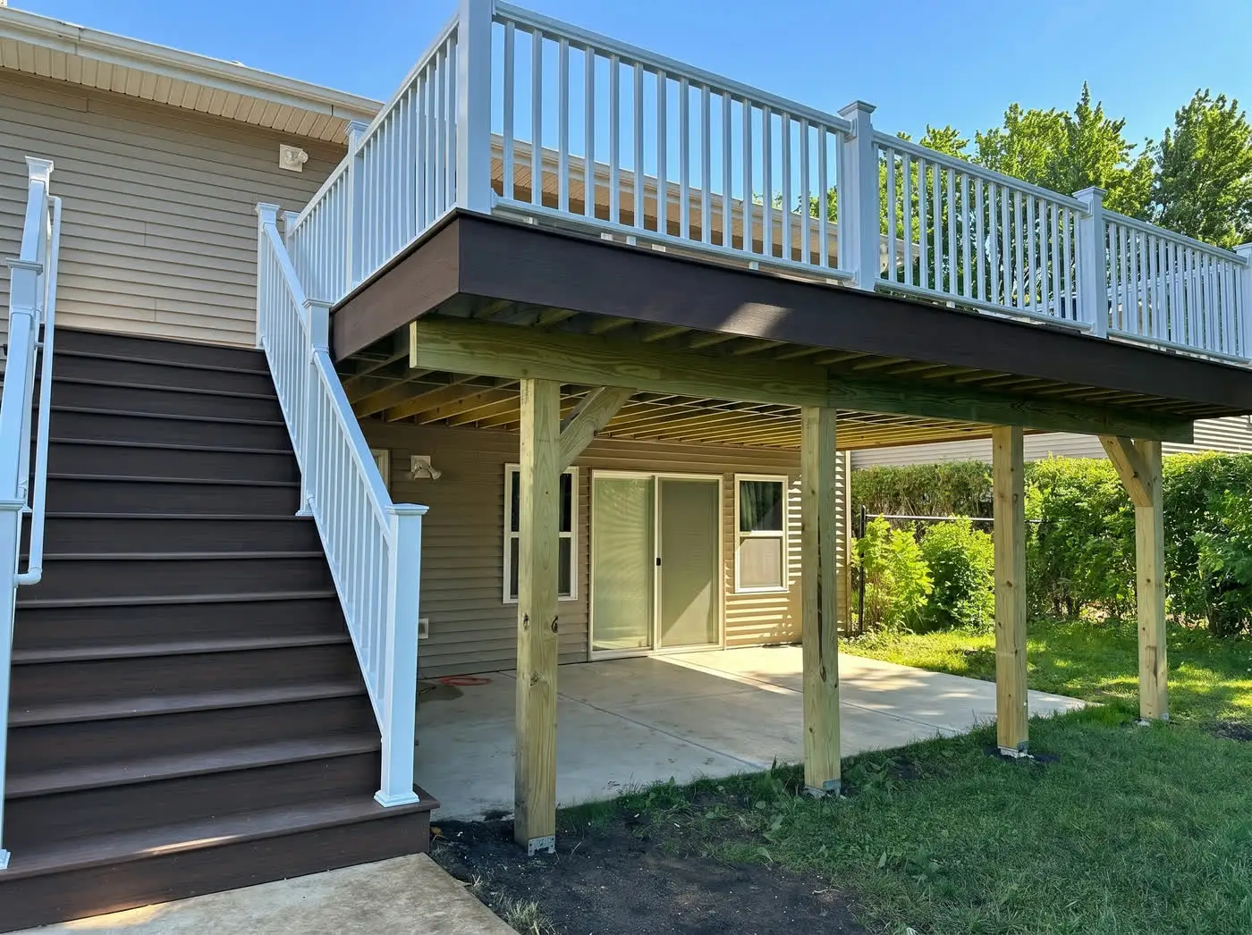 Elevated composite deck with white railings, dark fascia and a pressure-treated post-and-beam frame underneath