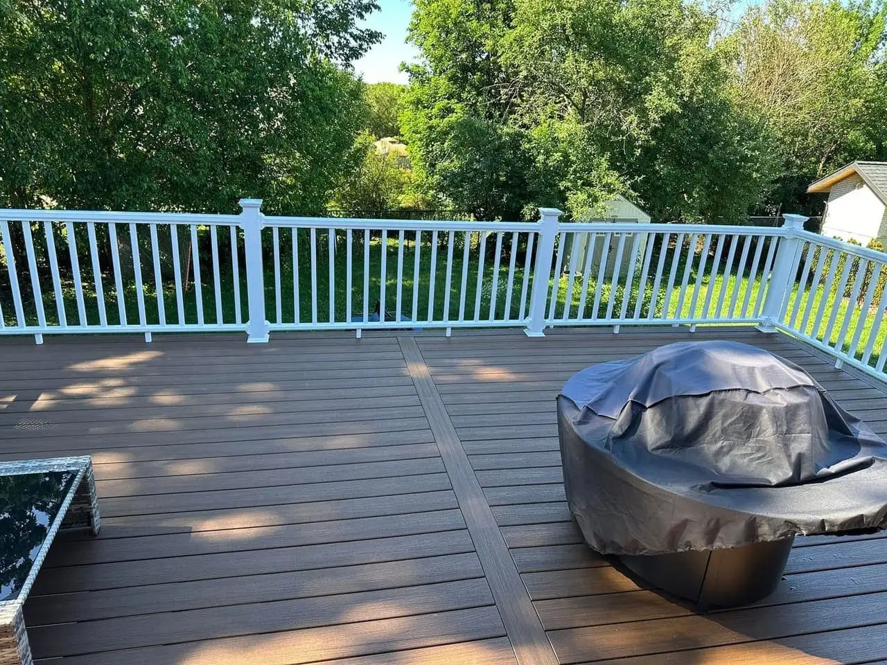 Brown composite deck with white railings, a covered gas grill and patio furniture