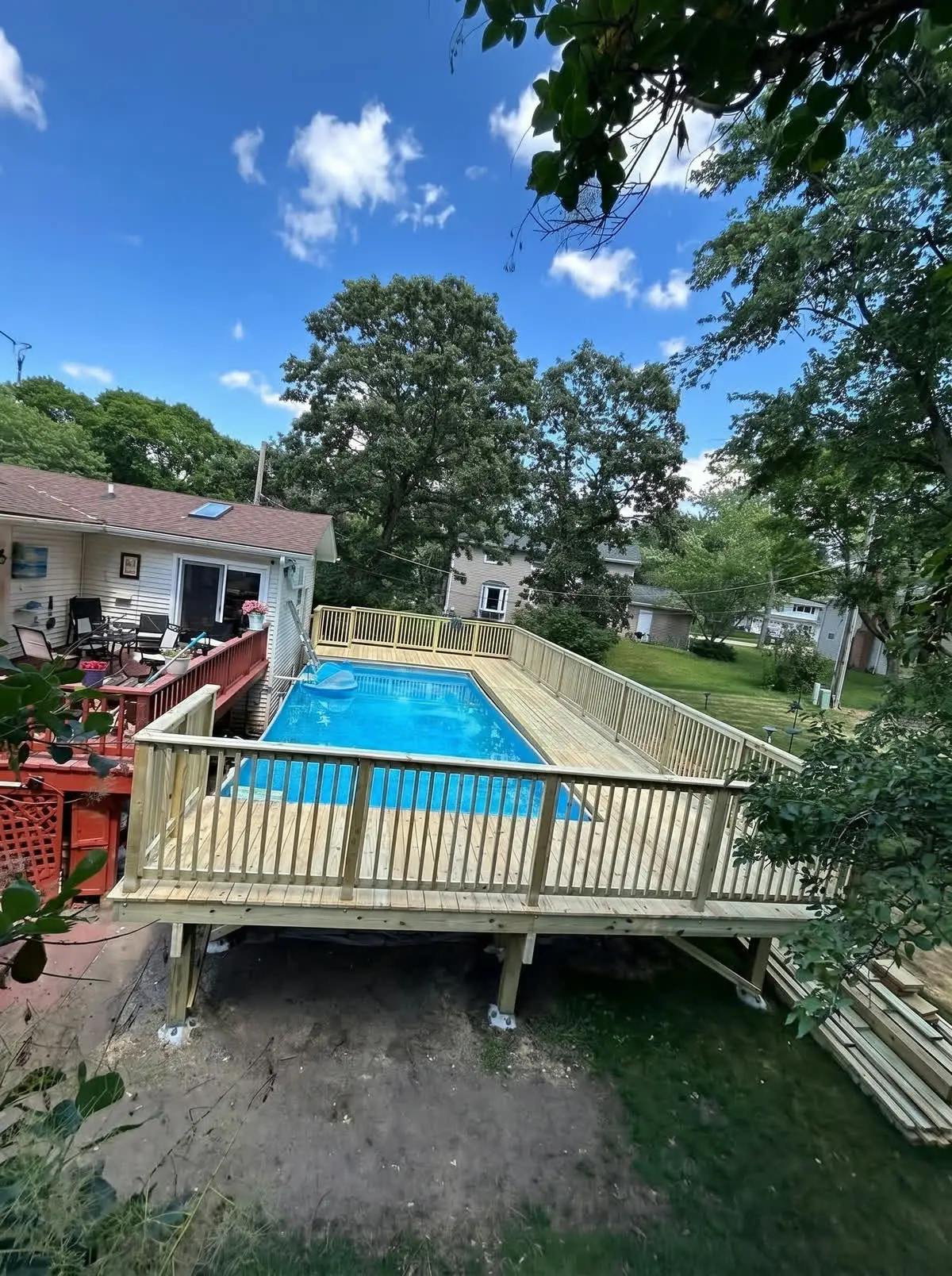 Wood deck running alongside an above-ground pool in a fenced backyard