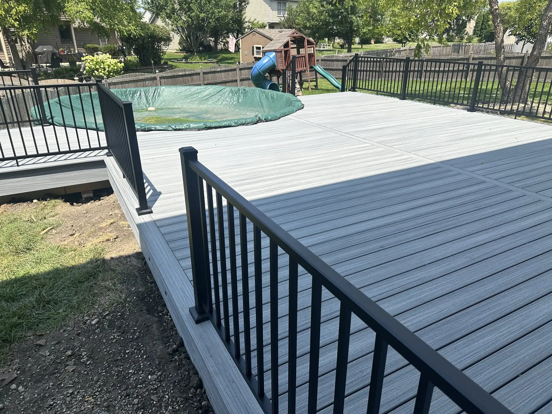 Grey composite pool deck with black aluminum railings wrapping an above-ground pool