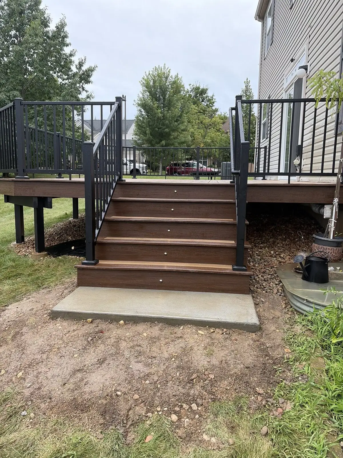 Warm brown composite deck stairs with black aluminum railing, landing on a concrete pad