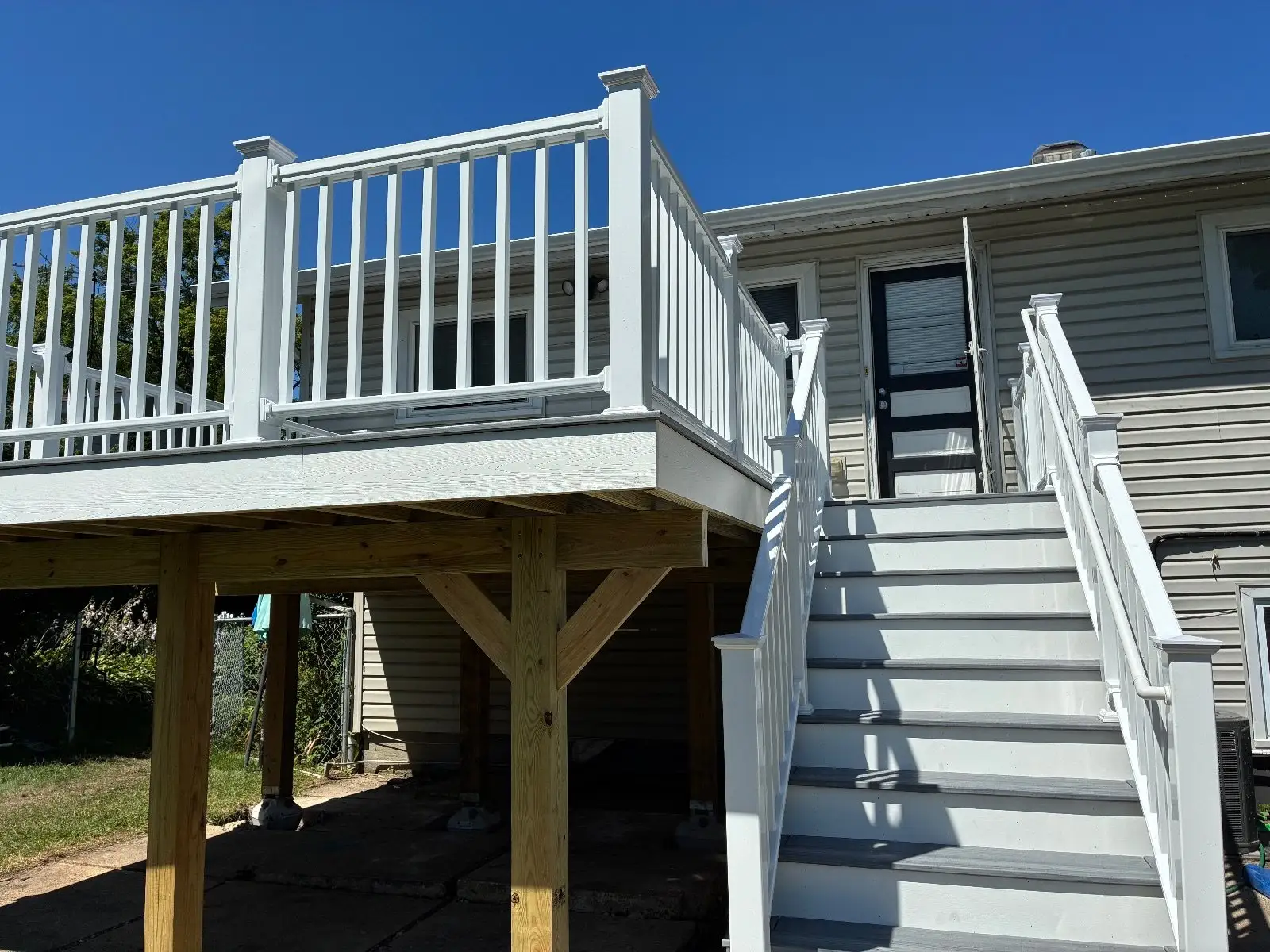 Elevated grey Trex Foggy Wharf deck with white railing and a full stair run, seen from the patio below