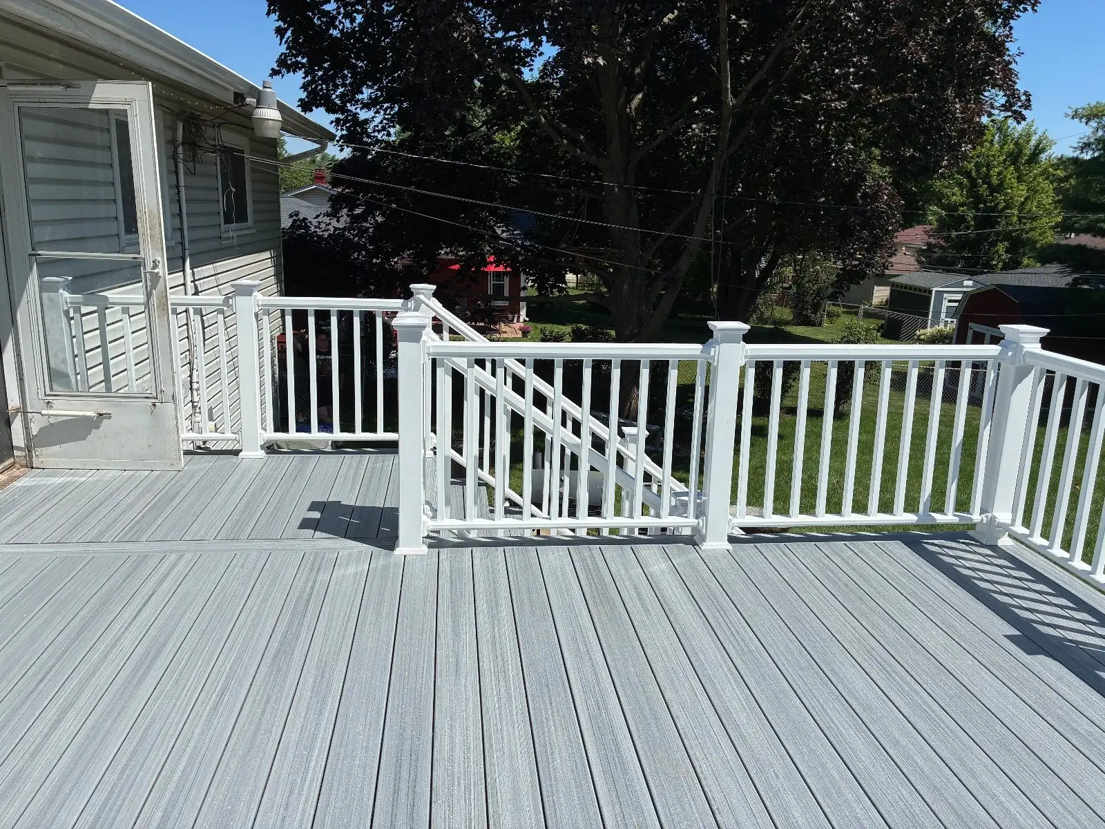 Wide grey composite deck surface at the kitchen door with white railing on three sides