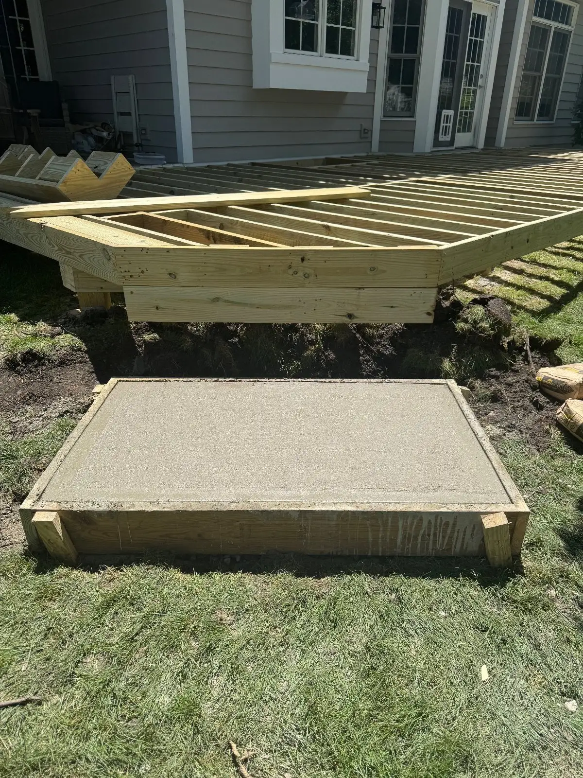 New deck frame in progress with a freshly poured concrete landing pad