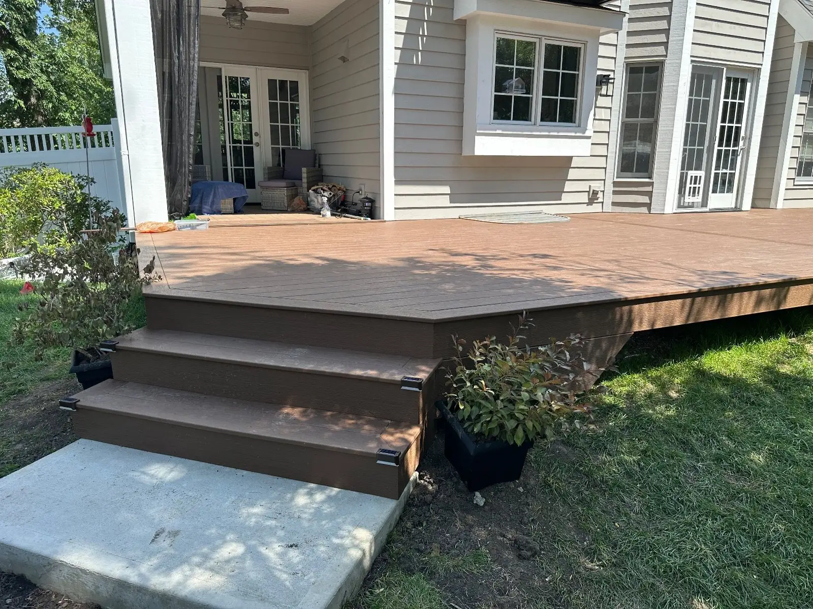 Corner steps down from the brown composite deck to a concrete pad, a planter beside them