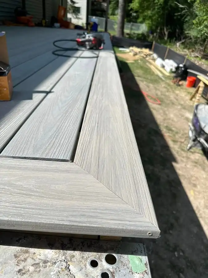 Grey composite deck boards being laid over a new pressure-treated frame during a build