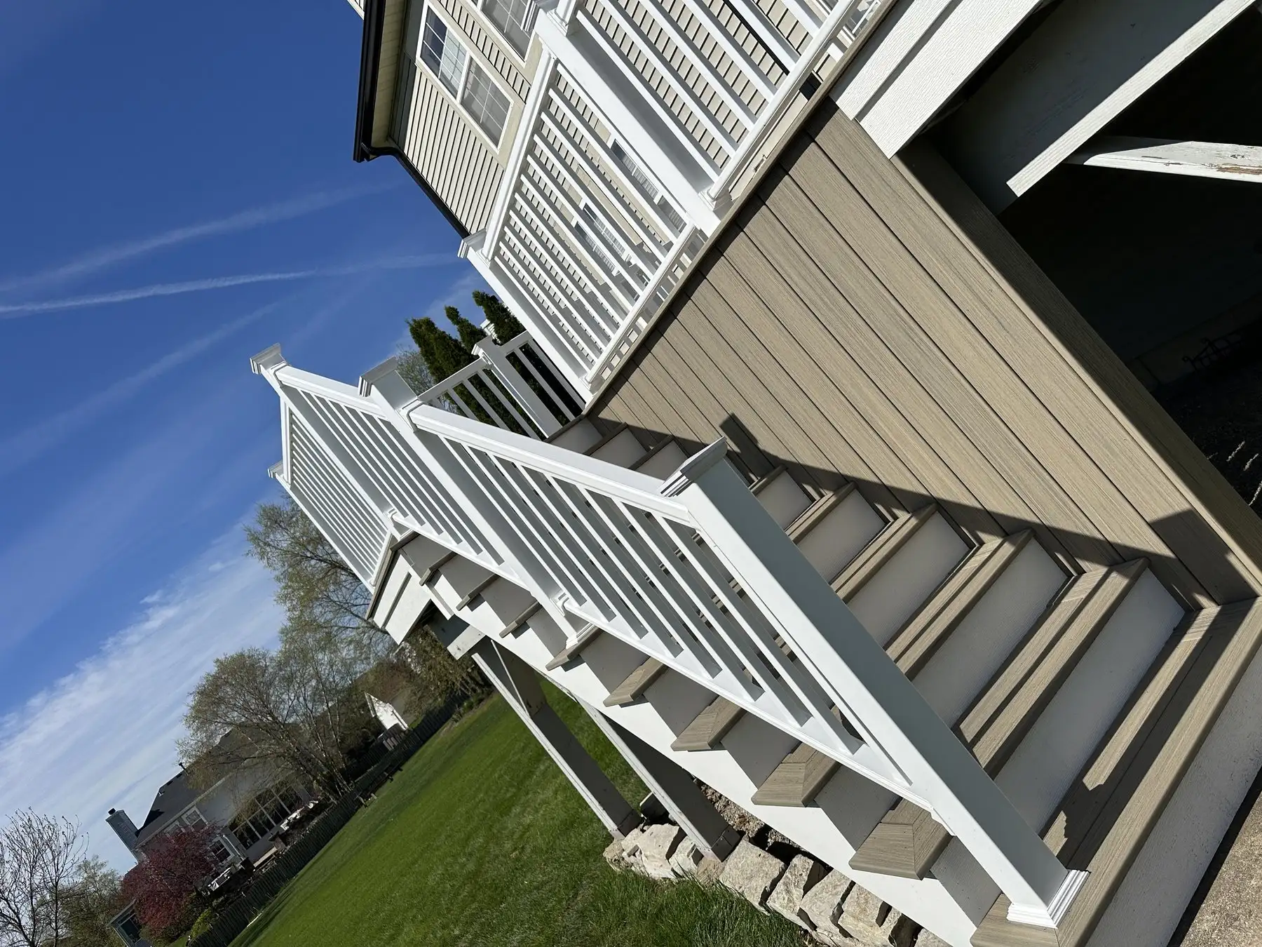 White deck railing running down a full staircase against a clear blue sky