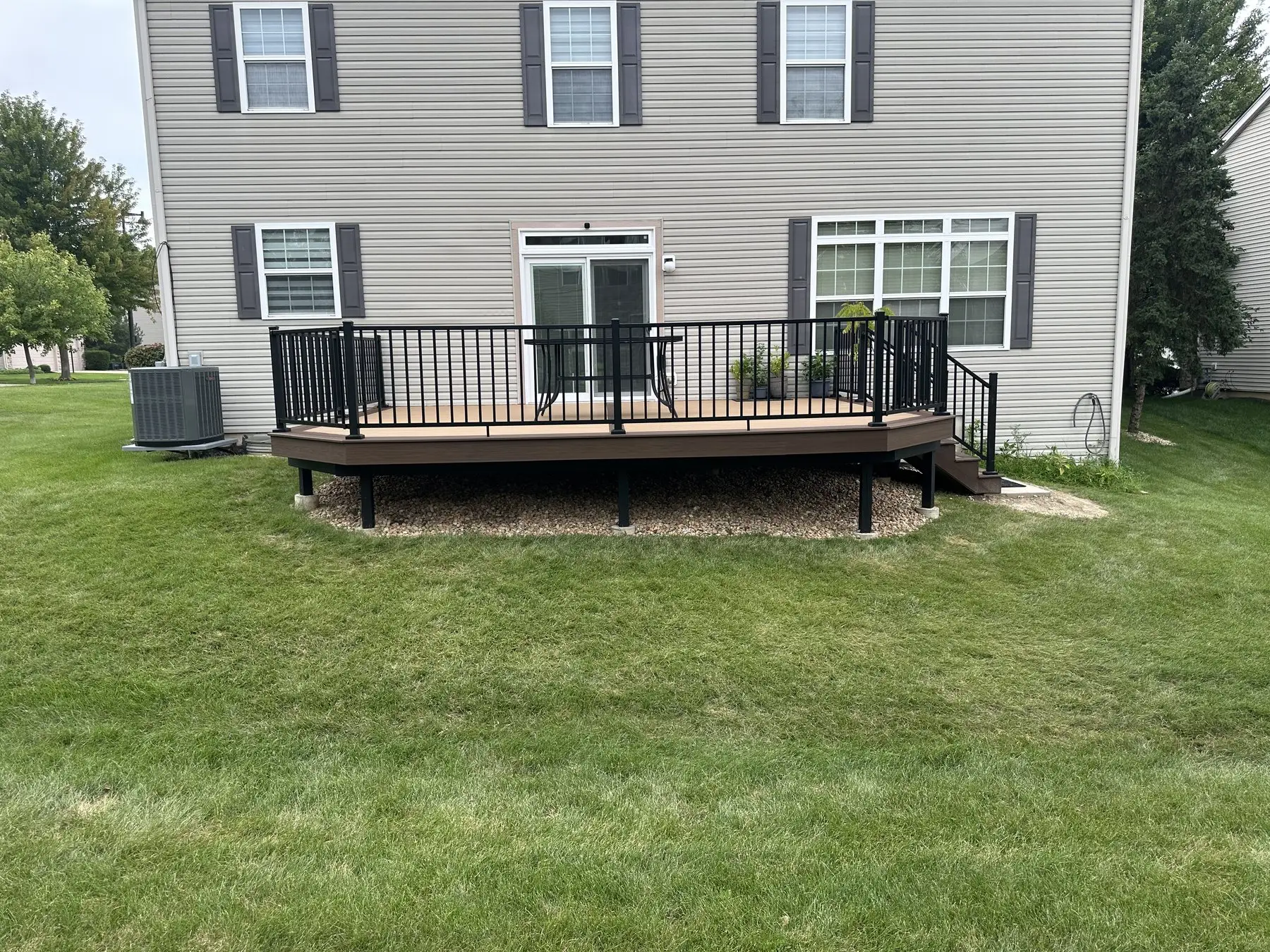 Warm brown composite deck with black aluminum railings and angled corners on the back of a two storey house
