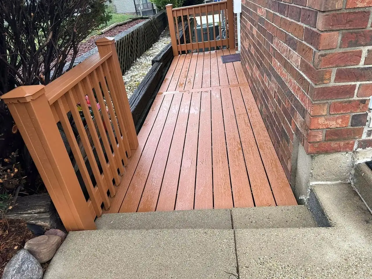 Warm stained wood deck with matching railing running along a red brick house wall